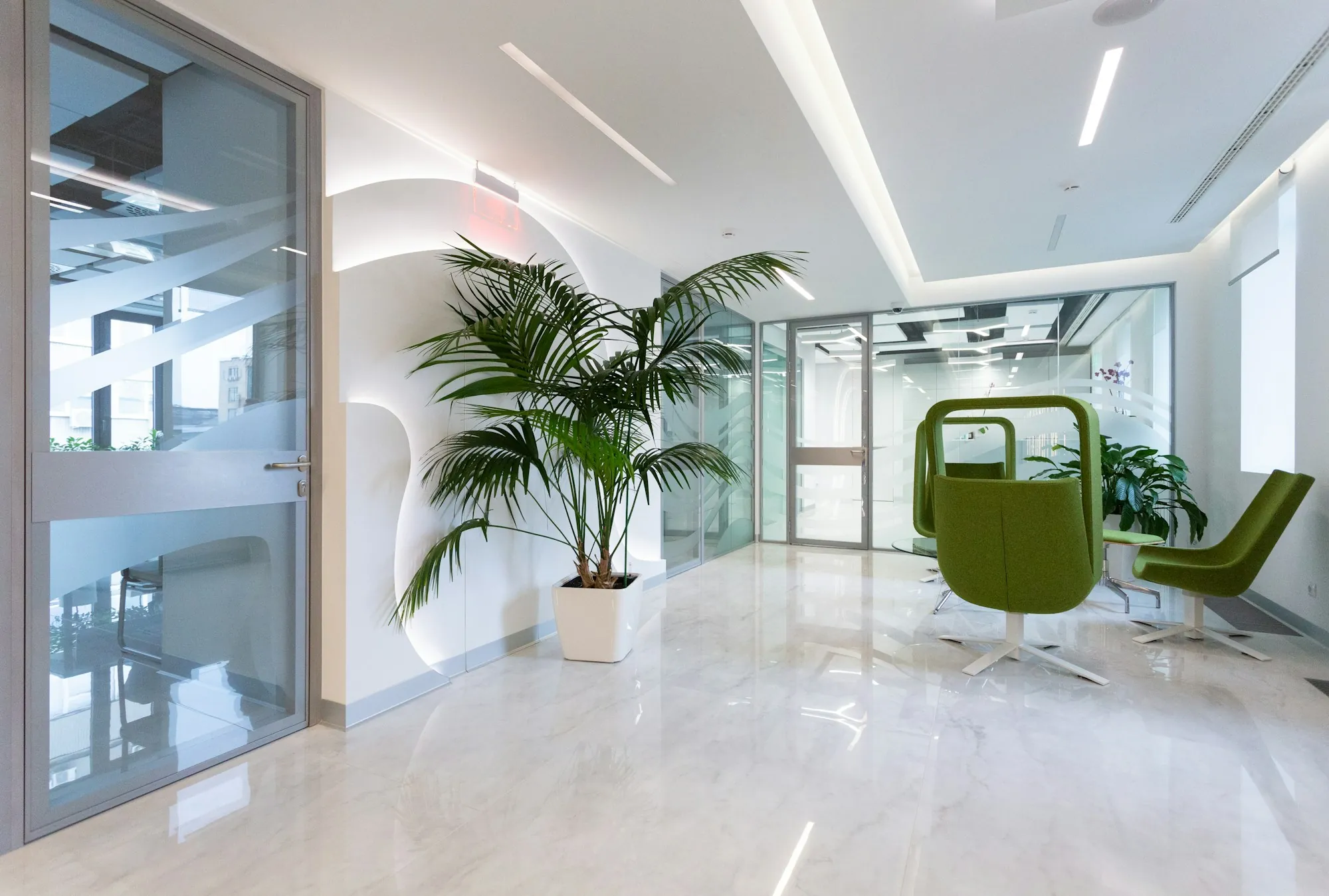 Clean white office lobby with plants and green chairs