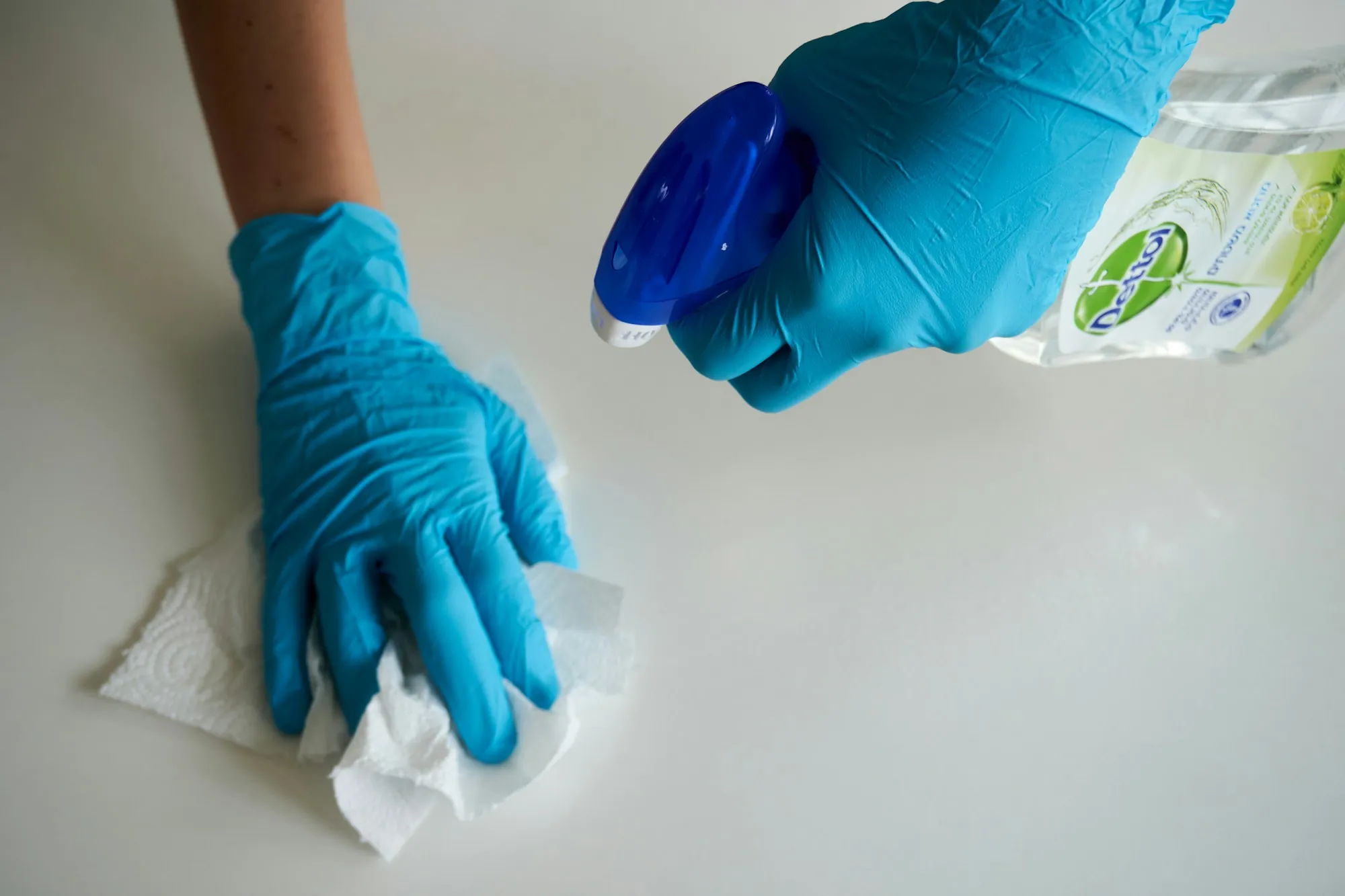 Gloved hand wiping a white counter with a paper towel and spray